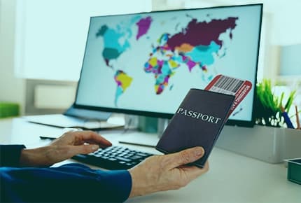 Person holding passport and ticket near computer showing world map, symbolizing how a visa management system simplifies complex processes and workflows.